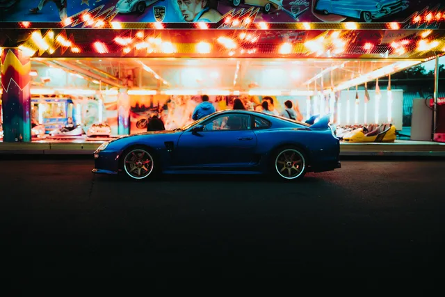 Blauer Toyota Supra vor einem leuchtenden Fahrgeschäft